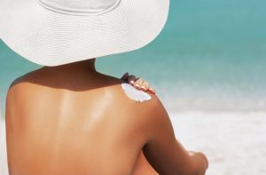 Woman at beach applying sunscreen to shoulder