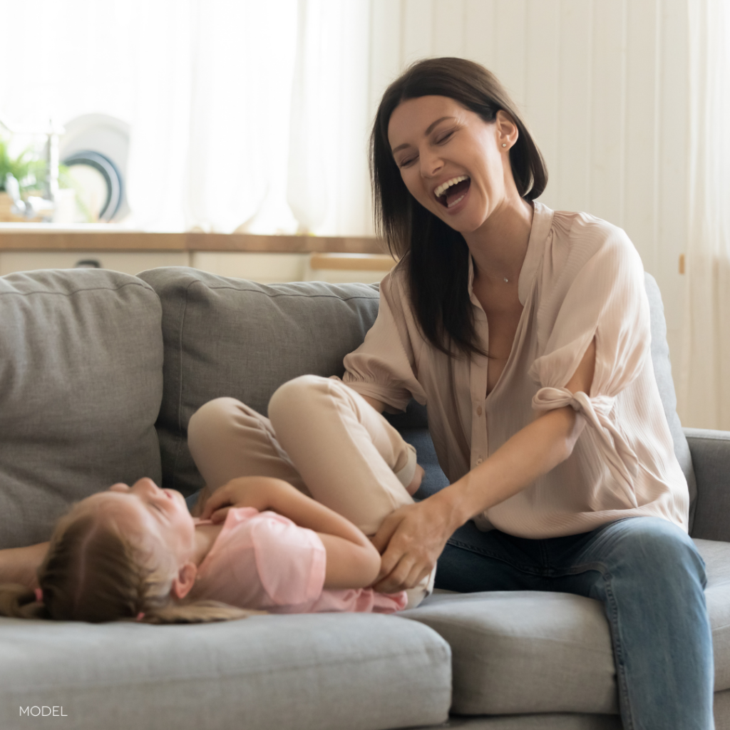 Mom on couch with young daughter, laughing